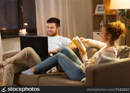 leisure and people concept - happy couple with laptop computer and book at home in evening. couple with laptop computer and book at home