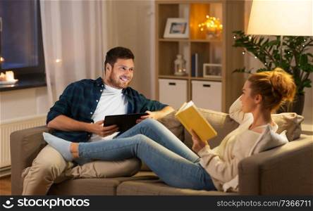 leisure and people concept - happy couple with tablet computer and book talking at home in evening. couple with tablet computer and book at home