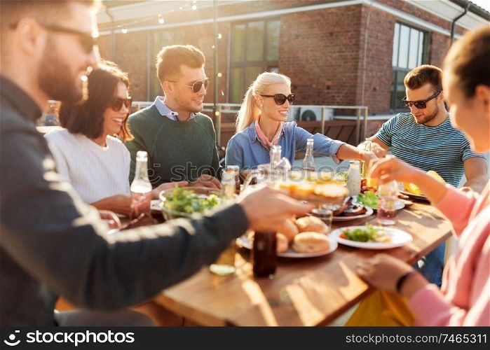 leisure and people concept - happy friends eating and drinking at barbecue party on rooftop. friends having dinner or bbq party on rooftop