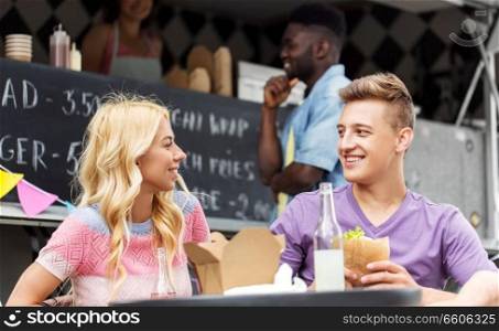 leisure and people concept - happy friends eating and talking at food truck. friends eating and talking at food truck