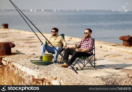 leisure and people concept - happy friends fishing and drinking beer on pier. happy friends fishing and drinking beer on pier