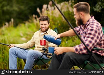 leisure and people concept - happy friends fishing and drinking tea from thermos outdoors. friends fishing and drinking tea from thermos
