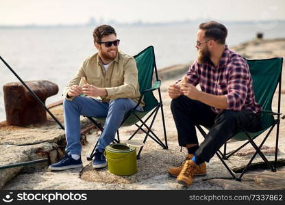 leisure and people concept - happy friends fishing and eating sandwiches on pier at sea. happy friends fishing and eating sandwiches