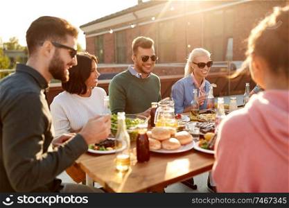 leisure and people concept - happy friends having dinner or barbecue party and eating on rooftop in summer. friends having dinner or bbq party on rooftop
