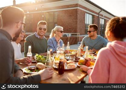 leisure and people concept - happy friends having dinner or barbecue party on rooftop in summer. friends having dinner or bbq party on rooftop