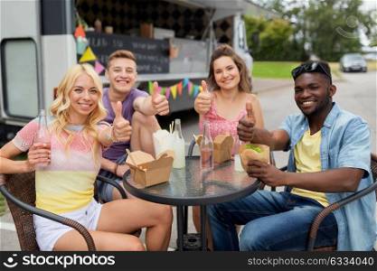 leisure and people concept - happy friends with drinks eating at food truck showing thumbs up. happy friends with drinks eating at food truck