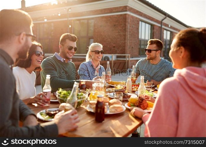 leisure and people concept - happy friends with drinks having dinner or barbecue party on rooftop. happy friends with drinks or bbq party on rooftop