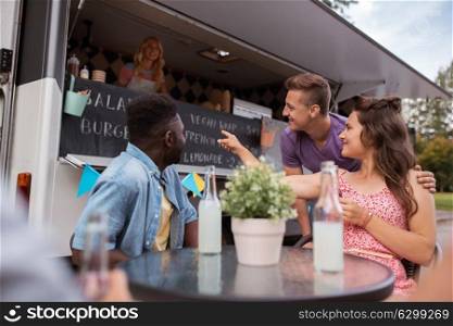 leisure and people concept - happy friends with drinks ordering at food truck. friends with drinks sitting at table at food truck