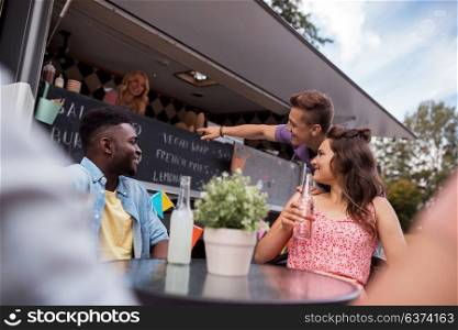 leisure and people concept - happy friends with drinks ordering at food truck. friends with drinks sitting at table at food truck