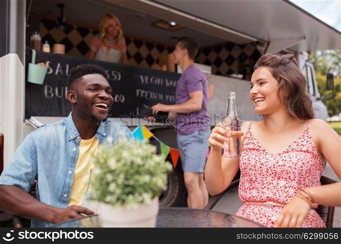 leisure and people concept - happy friends with drinks sitting at table at food truck. friends with drinks sitting at table at food truck