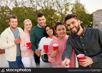leisure and people concept - happy friends with drinks taking selfie at rooftop party in summer. friends with drinks taking selfie at rooftop party