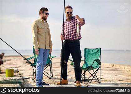 leisure and people concept - happy friends with fish and fishing rods on pier at sea. happy friends with fish and fishing rods on pier