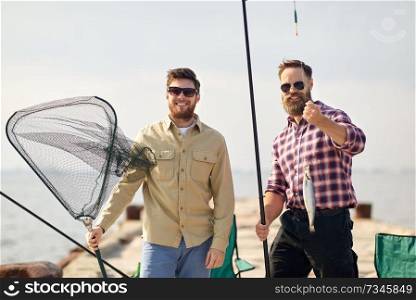 leisure and people concept - happy friends with fishing rod, fish and tackle on pier at sea. friends with fishing rod, fish and tackle on pier