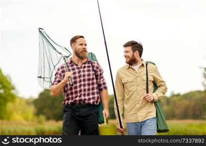 leisure and people concept - happy friends with fishing rods and scoop net walking along pier at lake or river. friends with fishing rods and net at lake or river