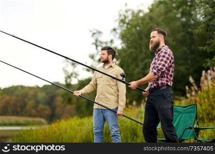 leisure and people concept - happy friends with fishing rods at lake or river. friends with fishing rods at lake or river