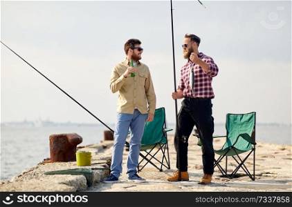 leisure and people concept - happy friends with fishing rods, fish and beer talking on pier at sea. happy friends with fishing rods and beer on pier