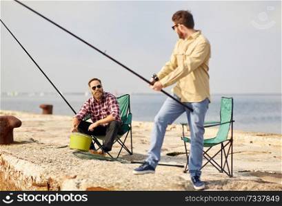 leisure and people concept - happy friends with fishing rods on pier at sea. happy friends with fishing rods on pier