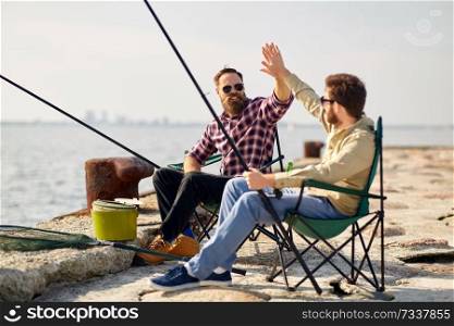 leisure and people concept - happy friends with fishing rods on pier at sea. happy friends with fishing rods on pier