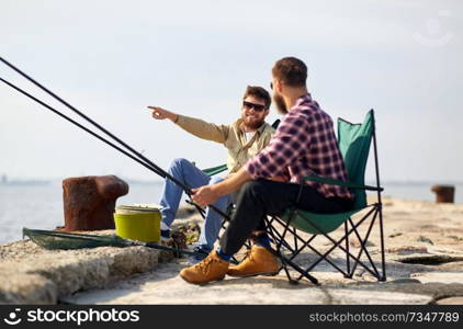 leisure and people concept - happy friends with fishing rods on pier at sea. happy friends with fishing rods on pier