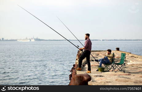 leisure and people concept - happy friends with fishing rods on pier at sea. happy friends with fishing rods on pier