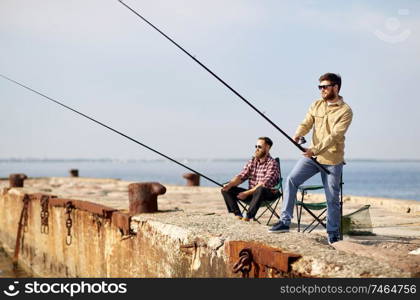 leisure and people concept - happy friends with fishing rods on pier at sea. happy friends with fishing rods on pier