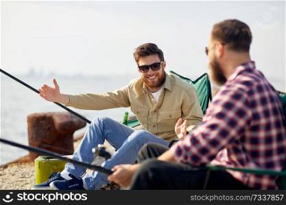 leisure and people concept - happy male friends with rods on pier at sea telling stories about fishing. happy male friends with rods talking about fishing