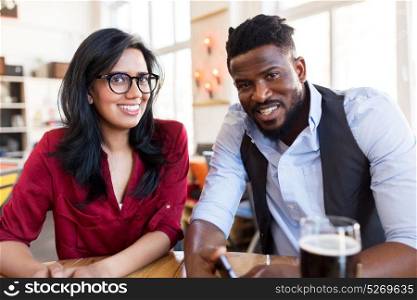 leisure and people concept - happy man and woman with smartphone and drinks at bar or restaurant. happy man and woman with smartphone at bar