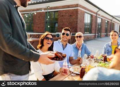 leisure and people concept - happy party host offering meat to his friends at barbecue party on rooftop in summer. friends at barbecue party on rooftop in summer