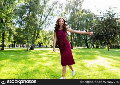 leisure and people concept - happy smiling beautiful woman with long wavy hair walking along summer park. happy smiling woman walking along summer park