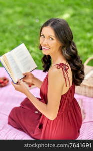 leisure and people concept - happy smiling woman sitting on picnic blanket and reading book at summer park. happy woman reading book at picnic in summer park