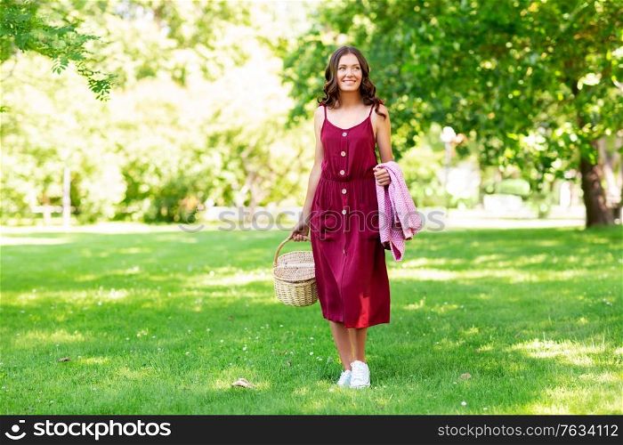 leisure and people concept - happy smiling woman with picnic basket and blanket at summer park. happy woman with picnic basket and blanket at park