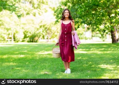 leisure and people concept - happy smiling woman with picnic basket and blanket at summer park. happy woman with picnic basket and blanket at park