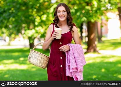 leisure and people concept - happy smiling woman with picnic basket, coffee cup and blanket at summer park. happy woman with picnic basket and coffee at park