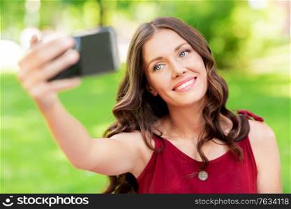leisure and people concept - happy smiling woman with smartphone taking selfie at summer park. happy woman with smartphone taking selfie at park