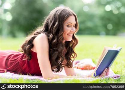 leisure and people concept - happy smiling young woman reading book at picnic in summer park. happy smiling woman reading book at summer park