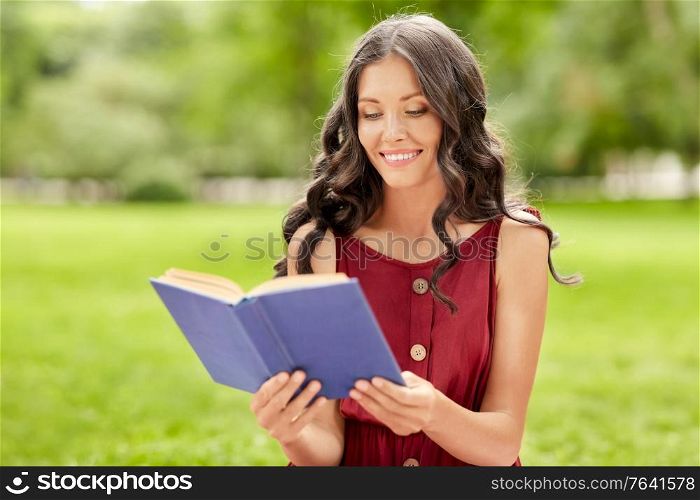 leisure and people concept - happy smiling young woman reading book at summer park. happy smiling woman reading book at park