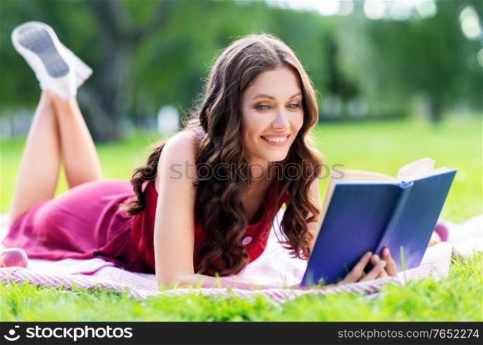 leisure and people concept - happy smiling young woman reading book at summer park. happy smiling woman reading book at summer park