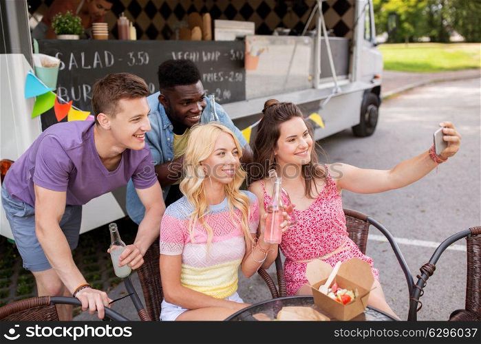 leisure and people concept - happy young friends with food and drinks and taking selfie at food truck. happy young friends taking selfie at food truck