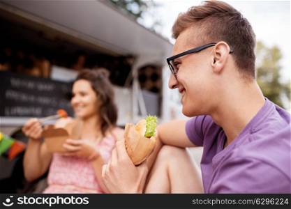 leisure and people concept - happy young man eating hamburger at food truck with friends. happy man eating hamburger at food truck