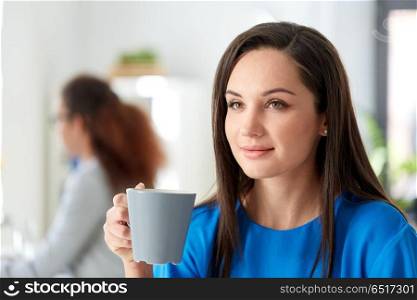leisure and people concept - happy young woman drinking coffee at office. happy woman drinking coffee at office. happy woman drinking coffee at office