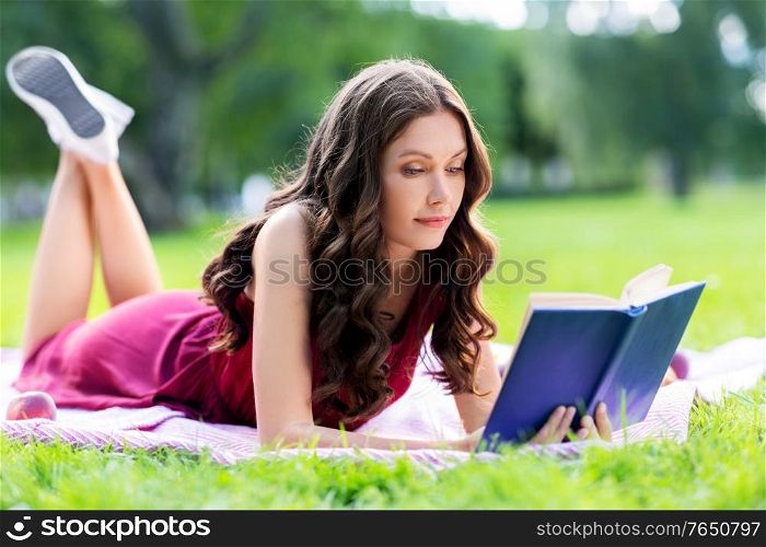 leisure and people concept - happy young woman reading book at picnic in summer park. happy young woman reading book at summer park