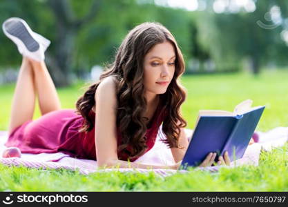 leisure and people concept - happy young woman reading book at picnic in summer park. happy young woman reading book at summer park