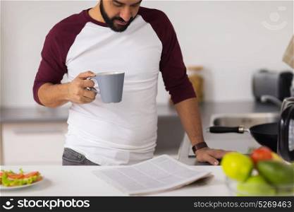 leisure and people concept - man drinking coffee for breakfast and reading newspaper at home kitchen. man with coffee reading newspaper at home kitchen