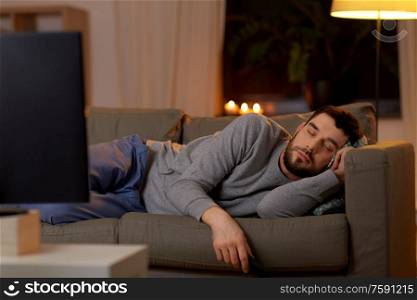 leisure and people concept - man sleeping on sofa with tv on at home at night. man sleeping on sofa with tv remote at home