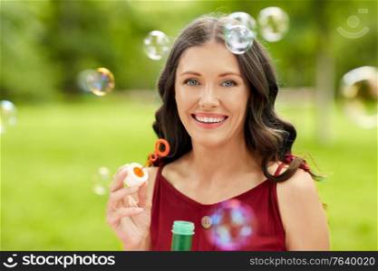 leisure and people concept - portrait of happy smiling woman blowing soap bubbles at summer park. happy woman blowing soap bubbles at summer park