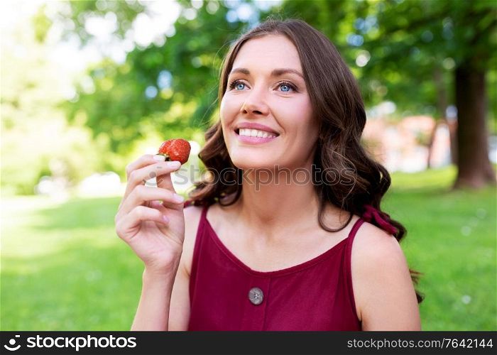 leisure and people concept - portrait of happy woman eating strawberry at summer park. happy woman eating strawberry at summer park