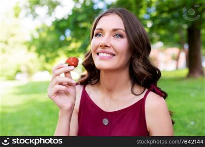 leisure and people concept - portrait of happy woman eating strawberry at summer park. happy woman eating strawberry at summer park