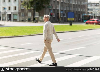 leisure and people concept - senior man walking along summer city crosswalk. senior man walking along city crosswalk