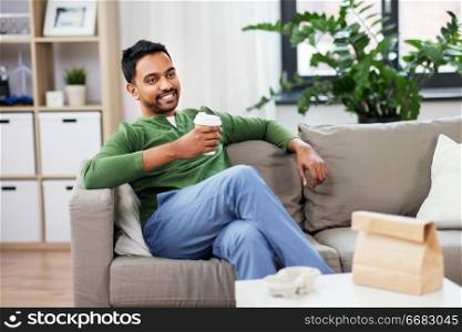 leisure and people concept - smiling indian man drinking takeaway coffee at home. happy indian man drinking takeaway coffee at home