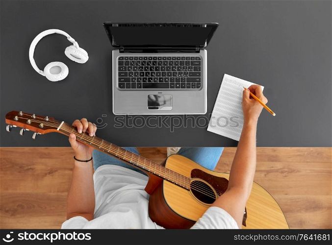 leisure and people concept - young man or musician with laptop computer and guitar writing to music book at table. man with guitar writing to music book at table